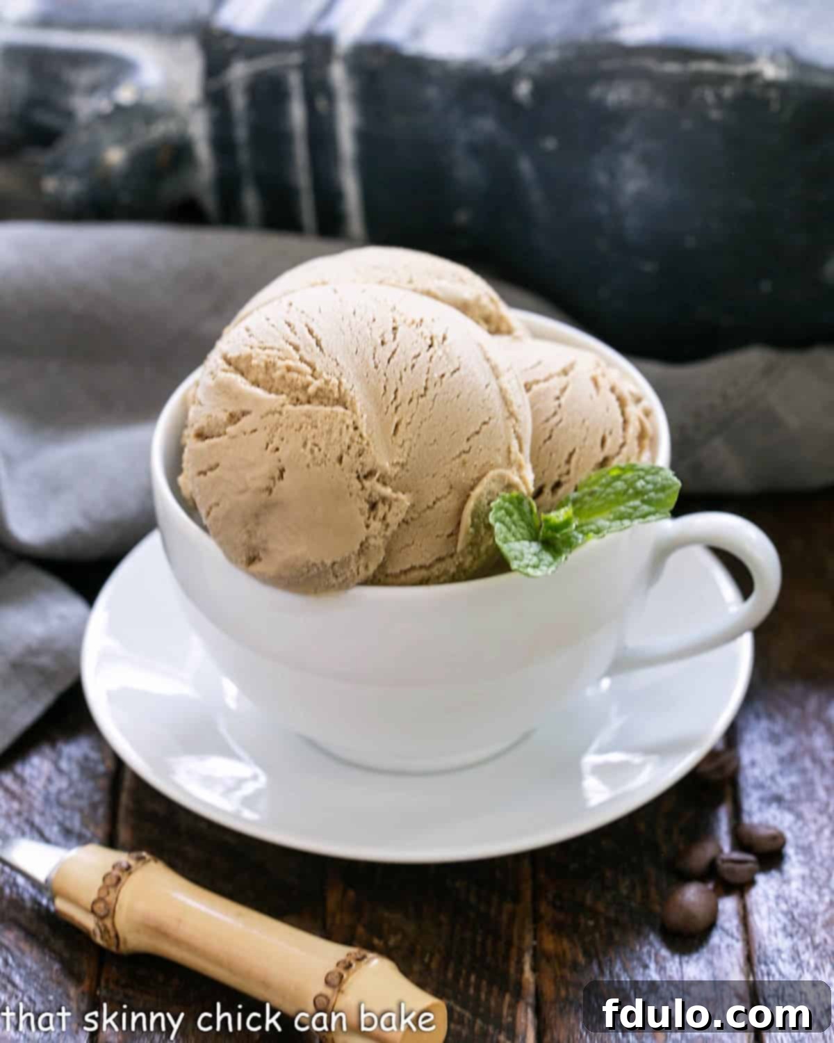 Three scoops of homemade coffee ice cream in a white tea cup, showcasing its rich brown color and creamy texture.