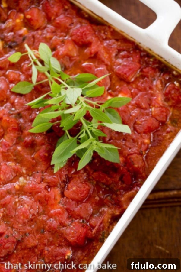 A pristine white casserole dish filled with baked Chicken Feta Casserole, garnished with a sprig of fresh basil, hot from the oven.