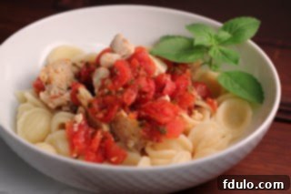 A large serving of Chicken Feta Casserole in a white bowl with a sprig of basil, ready for a delicious meal.