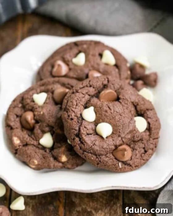 Freshly baked Triple Chocolate Fudge Cookies cooling on a wire rack, with some already on a plate, ready to be enjoyed.