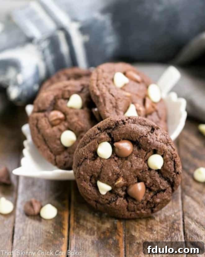 A generous serving of Triple Chocolate Fudge Cookies nestled in a decorative leaf-shaped bowl, with one perfectly baked cookie artfully leaning against the side, showcasing its rich, dark color and abundance of chocolate chips.