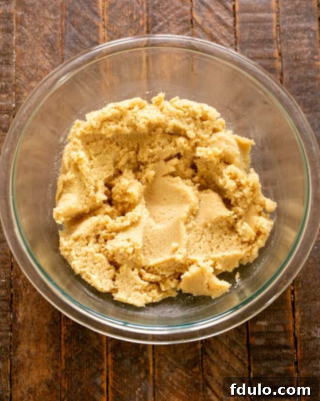Butter and sugars being creamed together in a mixing bowl with a hand mixer, forming a light and fluffy texture, the first step in making the cookie dough.