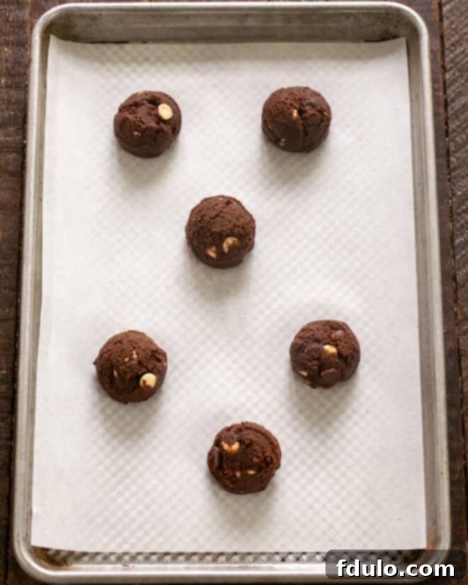 Portions of cookie dough being scooped evenly onto a parchment-lined baking sheet, spaced apart to allow for spreading during baking.
