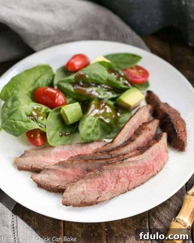 Red Wine, Soy, Balsamic Marinated Flank Steak on a white dinner plate with a spinach salad