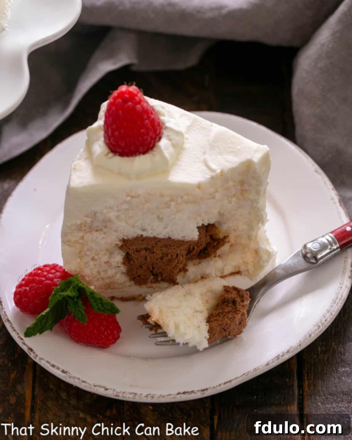 A slice of elegant mousse-filled angel food cake on a plate, revealing its creamy chocolate center, garnished with fresh raspberries and a fork.