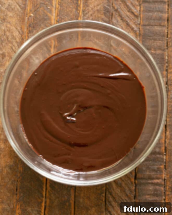 Stirring the melted chocolate and butter mixture until it is perfectly smooth and glossy.