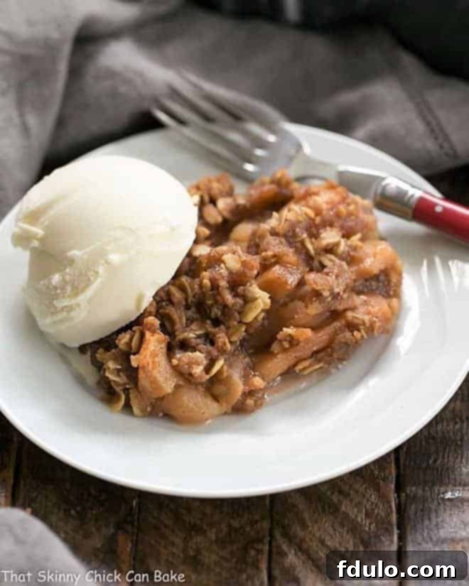 Easy Slow Cooker Apple Crisp with Oatmeal on a white dessert plate with a scoop of vanilla ice cream, showing its tender apple filling and crumbly topping.