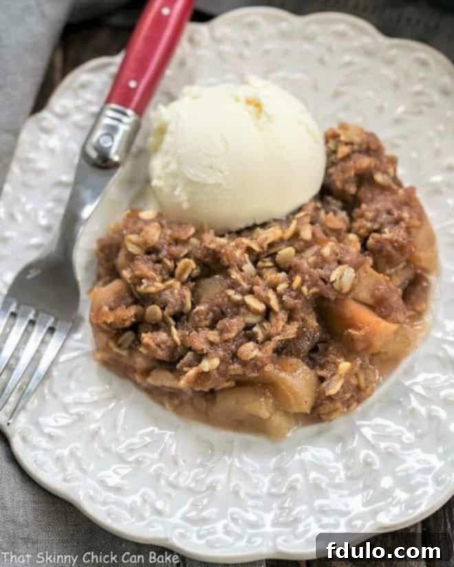 Easy Slow Cooker Apple Crisp with Oatmeal on a decorative white plate with vanilla ice cream and a red handled fork, highlighting its inviting texture.