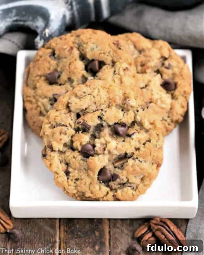 Loaded Cowboy Cookies Recipe - Buttery, chewy cookies with oats, chocolate chips, pecans and coconut A close-up shot of several loaded cowboy cookies on a white square plate, highlighting their golden-brown edges and the generous mix of oats, chocolate chips, pecans, and coconut within.