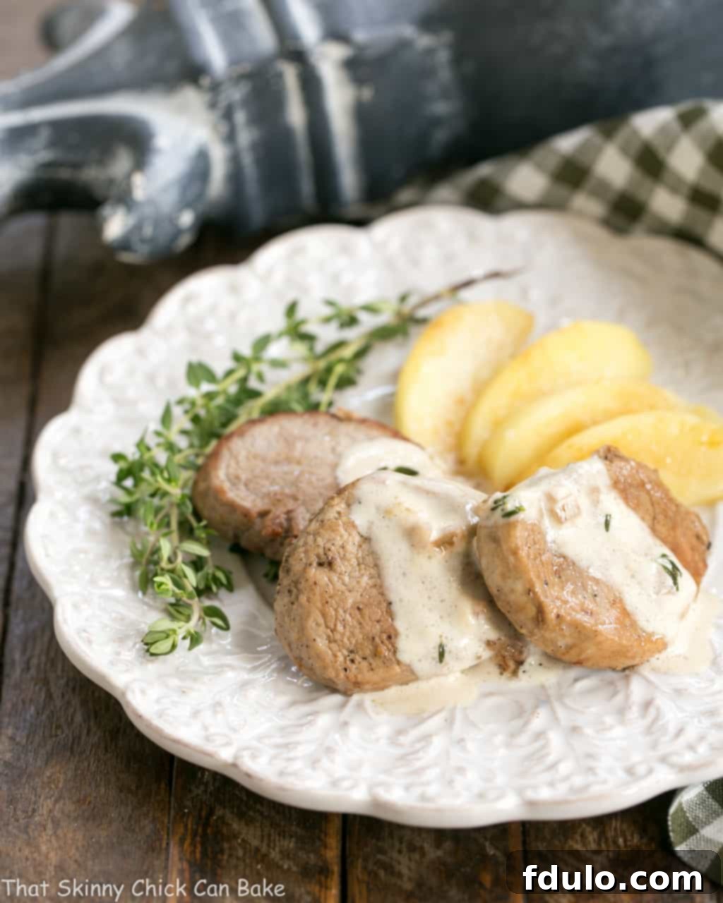 Apple Topped Pork Medallions with Calvados Cream Sauce on a white plate garnished with fresh thyme, ready to serve.