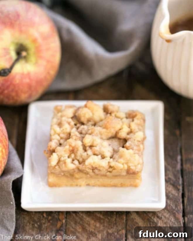 A single Caramel Apple Pie Bar on a square plate, featuring its golden-brown streusel topping and apple filling.