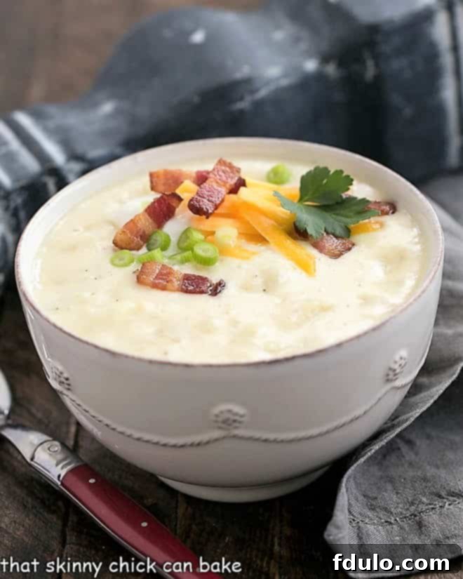 A white ceramic terrine filled with creamy Loaded Baked Potato Soup, elegantly garnished with a sprinkle of shredded cheese, crispy bacon bits, and fresh green chives, ready to be served.