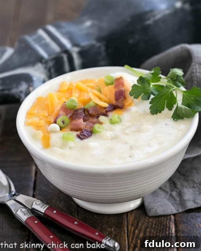 A side view of a generous serving of creamy Loaded Baked Potato Soup in a white ceramic soup bowl, accompanied by two elegant red-handled soup spoons, highlighting its inviting texture and rich garnishes.
