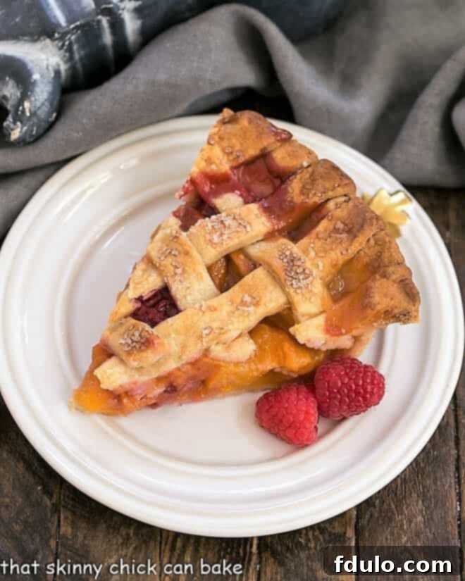 Overhead view of Peach pie recipe with raspberries slice on a white dessert plate.