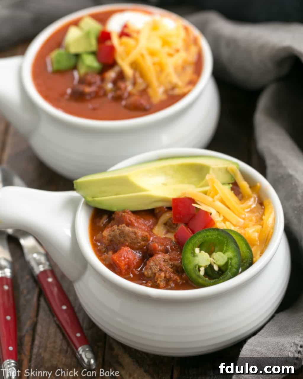 Two enticing bowls of Easy Black Bean Chili, generously garnished with melted shredded cheese and creamy avocado slices, highlighting its rich texture and delicious appeal as a hearty meal.