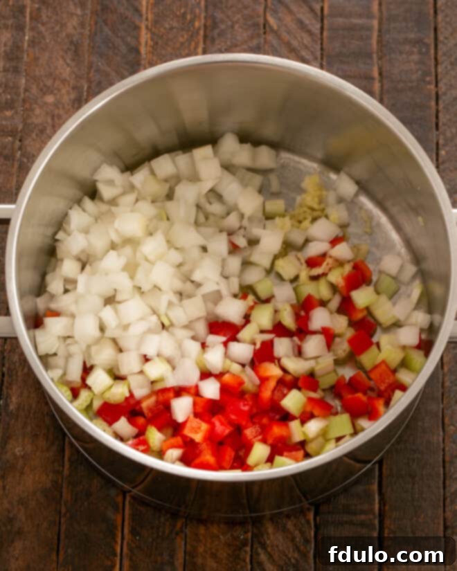 Freshly diced onions, red bell pepper, and celery cooking in olive oil in a large pot, beginning to soften and become fragrant, forming the aromatic base for the chili.