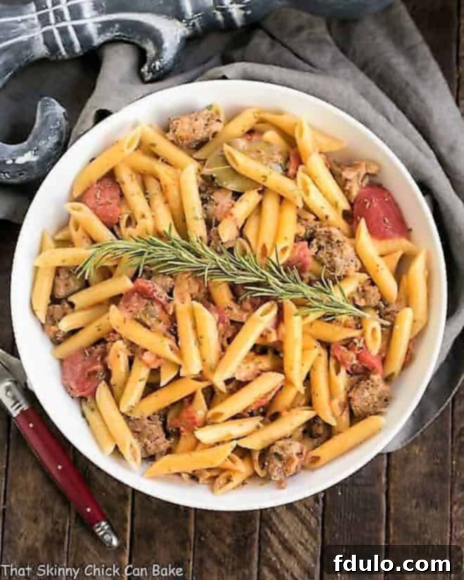 Delicious Creamy Italian Sausage Pasta in a white serving bowl with rosemary