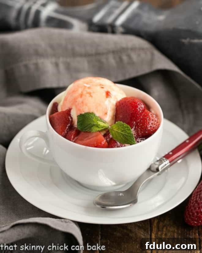 Cheesecake Ice Cream with Strawberry Sauce in a white teacup with a red handled spoon, garnished with fresh mint