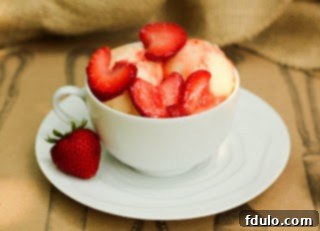 A bowl of cheesecake ice cream topped with fresh strawberry slices, with a spoon