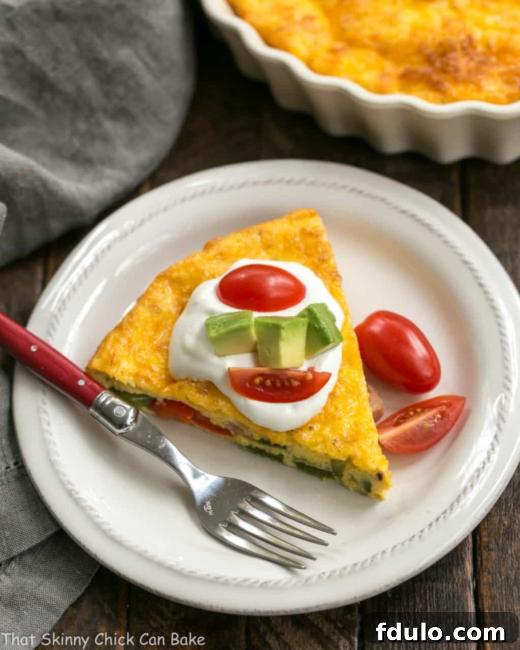 A perfectly portioned slice of Baked Denver Omelet on a white plate, ready to be enjoyed with a red handled fork.