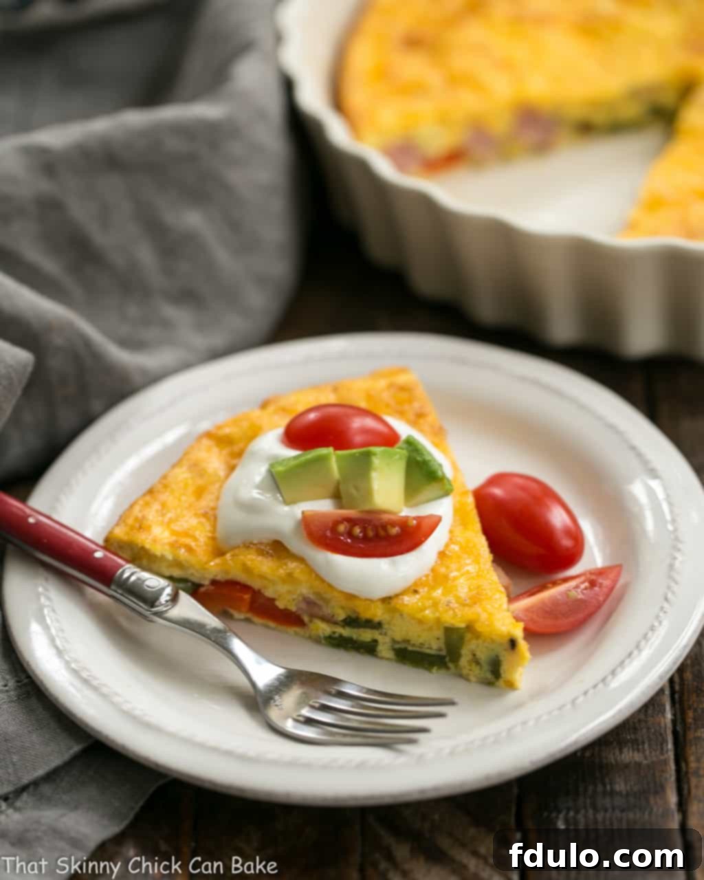 A slice of Baked Denver Omelet with the full casserole dish blurred in the background, emphasizing its hearty appeal.