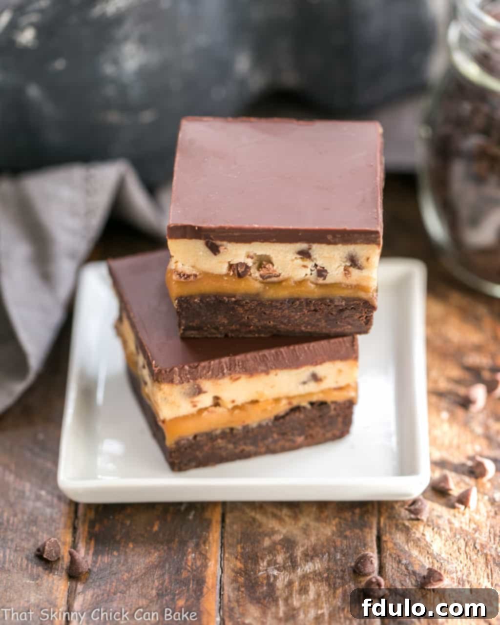 Cookie Dough Billionaire Bars stacked on a square white plate.