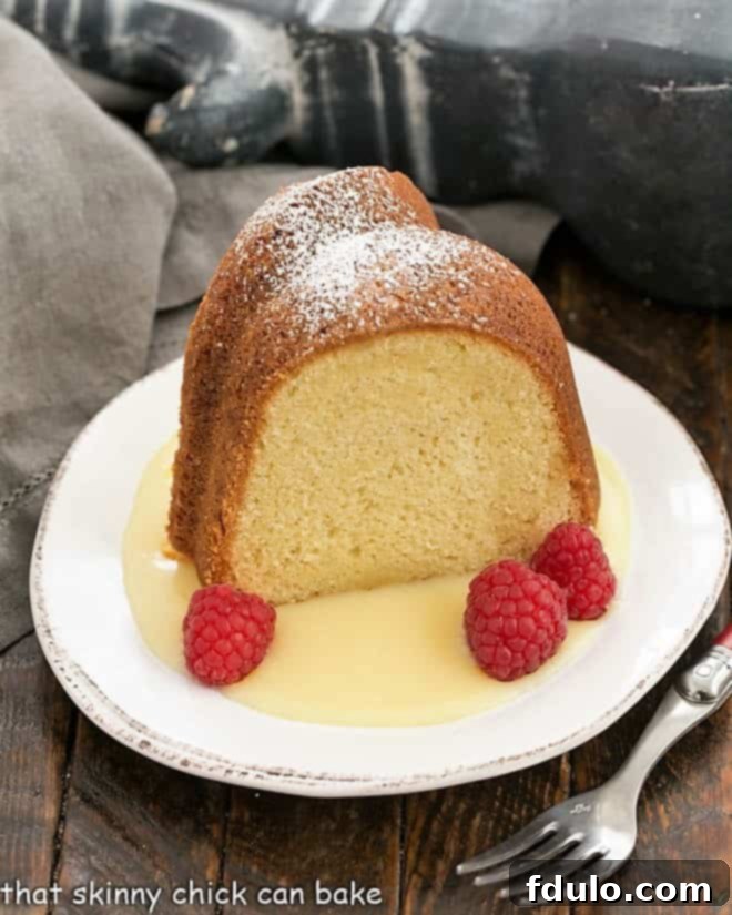 A beautifully presented slice of white chocolate pound cake on a dessert plate, drizzled with white chocolate sauce and garnished with fresh raspberries.