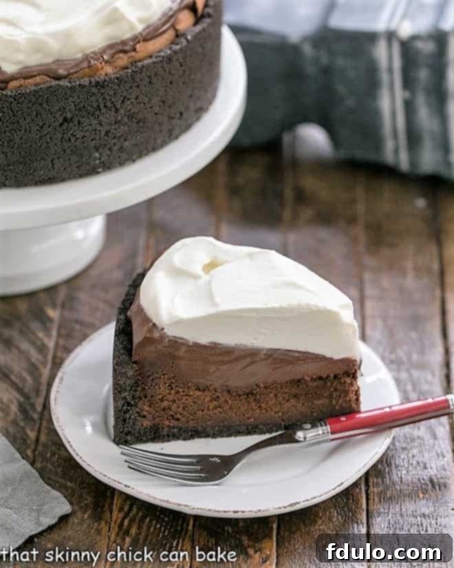 A pristine slice of Mississippi Mud Pie, perfectly layered, is presented on a white plate in front of a full cake stand, highlighting its rich chocolate and cream textures.