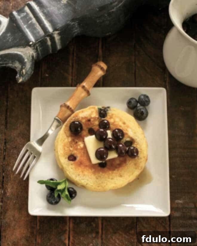 Stack of fluffy buttermilk pancakes topped with blueberry maple syrup and fresh blueberries.