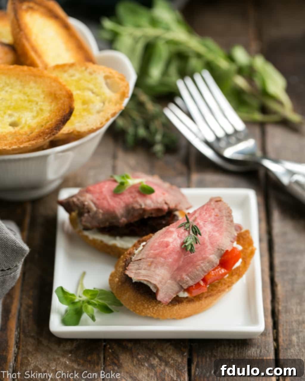 Gourmet Beef Crostini with Blue Cheese Spread and roasted red pepper on a square white appetizer plate, ready to serve.