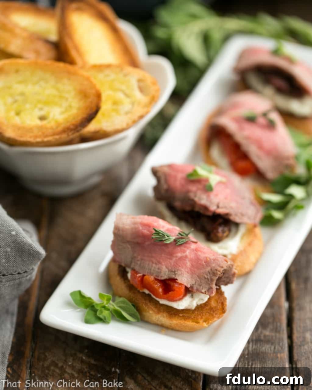 Line of Beef Crostini with Blue Cheese Spread and sun-dried tomatoes on a white platter, ready for a party.