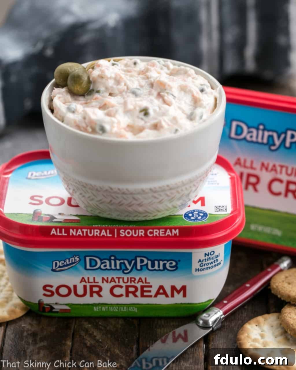 A bowl of Smoked Salmon Dip with Capers sitting on top of a container of sour cream, with a beautiful presentation.