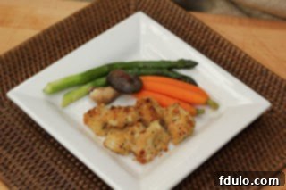 Overhead view of perfectly baked chicken nuggets arranged on a pristine white plate, accompanied by vibrant green and orange vegetables, highlighting a balanced, appealing meal.