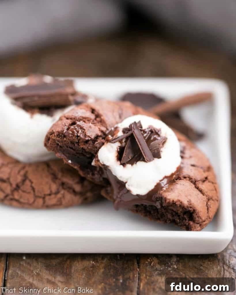 A close-up view of a Marshmallow Topped Hot Cocoa Cookie, broken open to reveal its chewy, chocolatey interior and soft marshmallow center, inviting a taste.