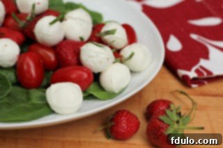 White oval platter of mozzarella, tomato and strawberry salad, garnished with fresh basil