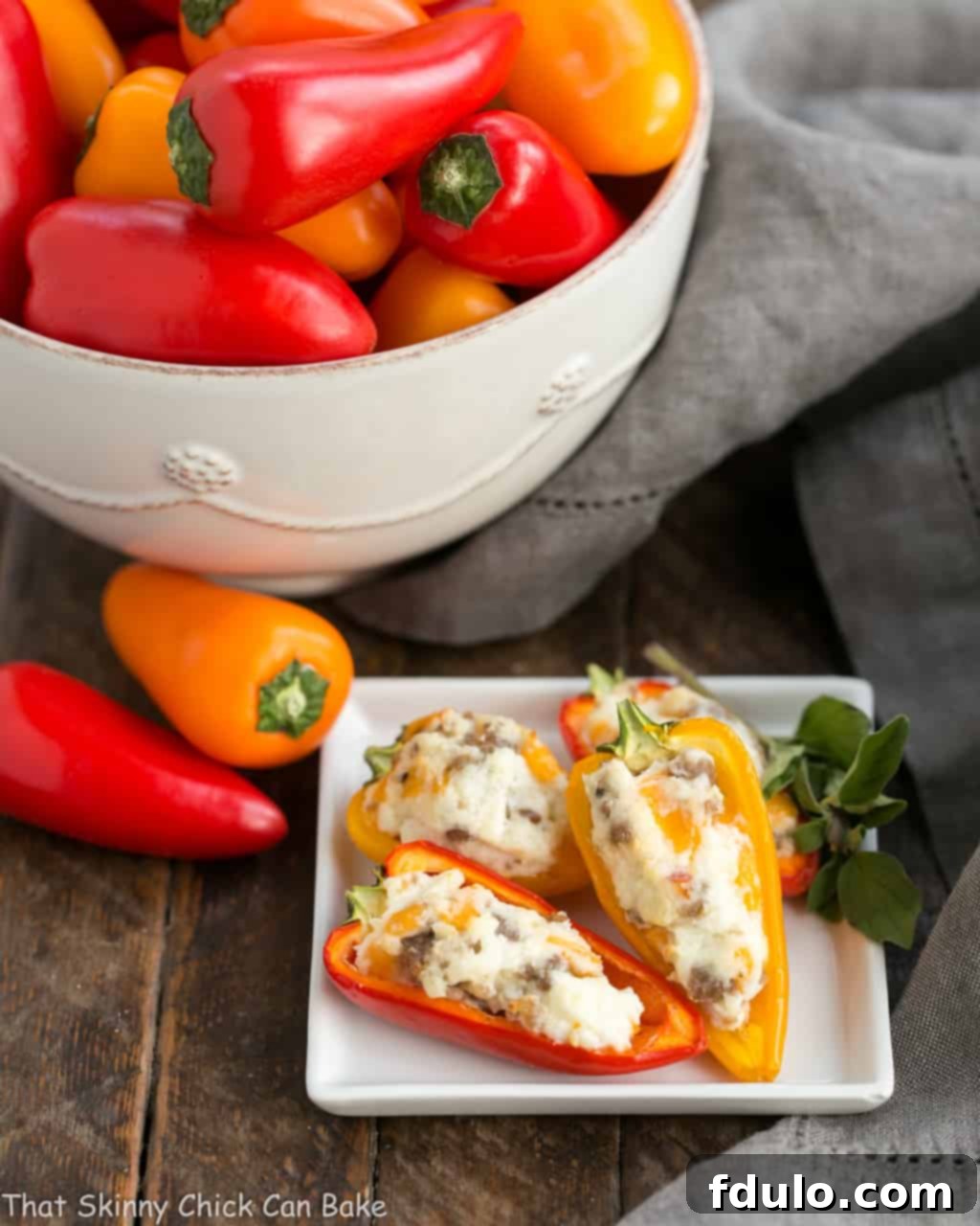 Irresistible Cream Cheese Stuffed Mini Peppers 2 Delicious cream cheese stuffed mini peppers with sausage on a square white plate, with a bowl of fresh mini peppers in the background.