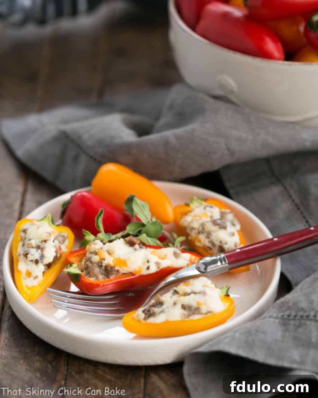 Irresistible Cream Cheese Stuffed Mini Peppers 4 Close-up of a single cream cheese stuffed mini pepper with sausage on a round white plate, with a red-handled fork.