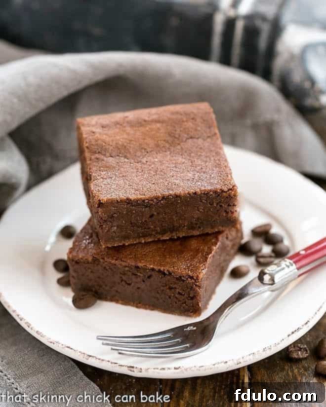 Kahlua Brownies on a round white plate with coffee beans and a fork, emphasizing their rich, fudgy texture.