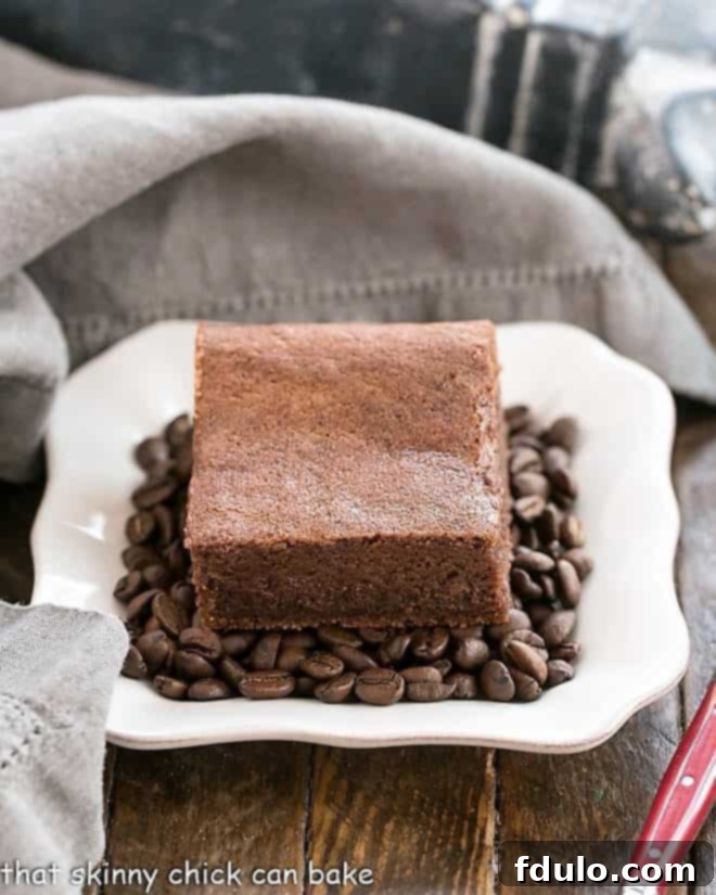 A close-up of Kahlua Brownies resting on a bed of coffee beans on a square white plate, highlighting their moist, dense interior.