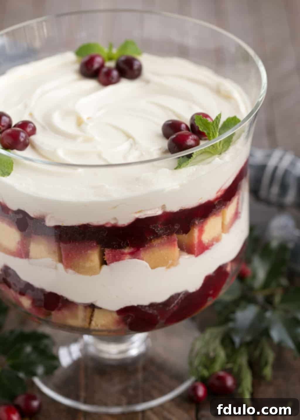 Cranberry Cheesecake Trifle is a delicious semi-homemade dessert that's a take on a traditional English trifle! This easy trifle recipe is a snap to prepare. #desserts #trifle #holidayrecipes A vibrant Cranberry Cheesecake Trifle beautifully layered in a clear glass trifle bowl, showcasing its festive colors.
