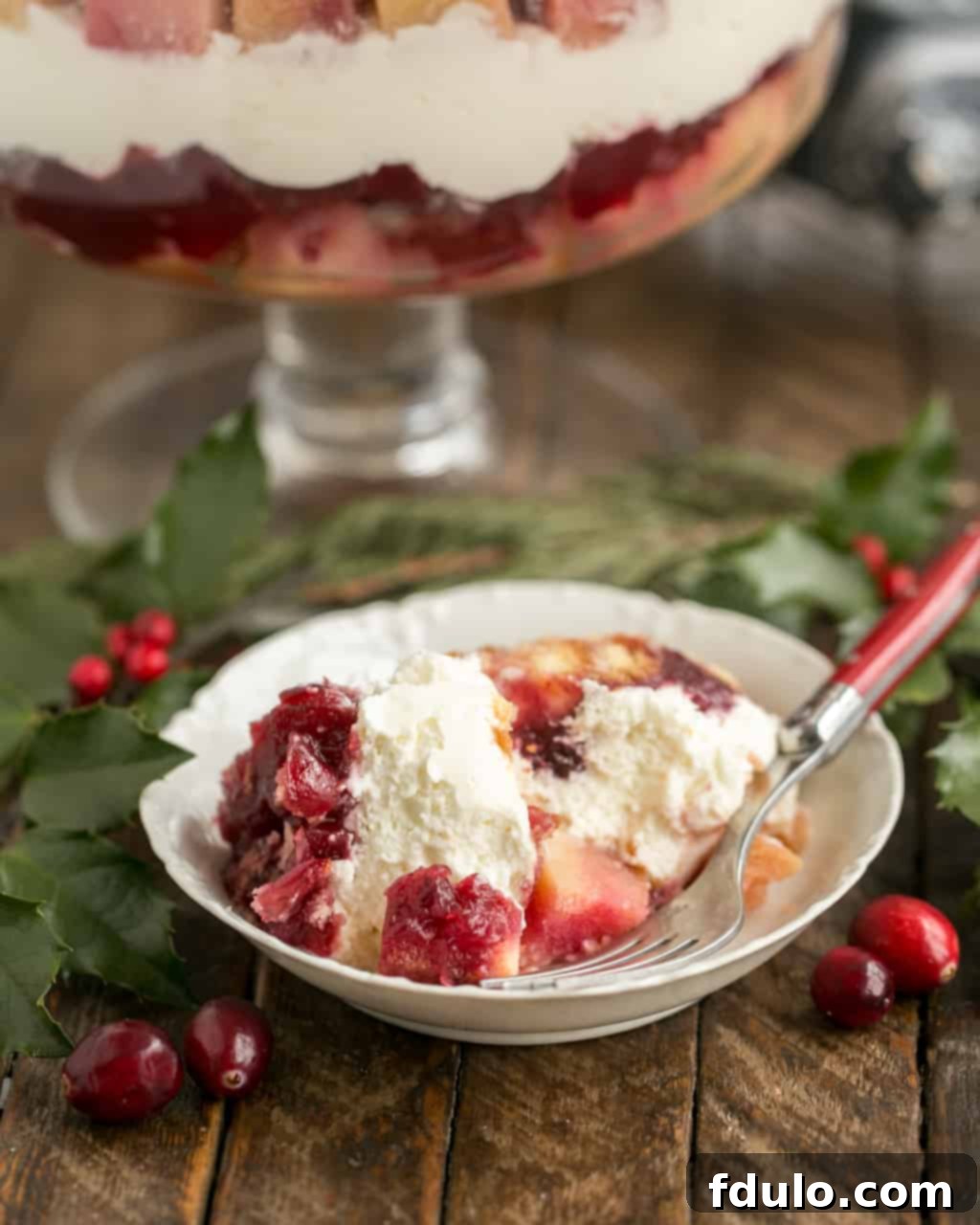 Cranberry Cheesecake Trifle is a delicious semi-homemade dessert that's a take on a traditional English trifle! This easy trifle recipe is a snap to prepare. #desserts #trifle #holidayrecipes A serving of Cranberry Cheesecake Trifle in a white bowl with a fork, ready to be enjoyed.