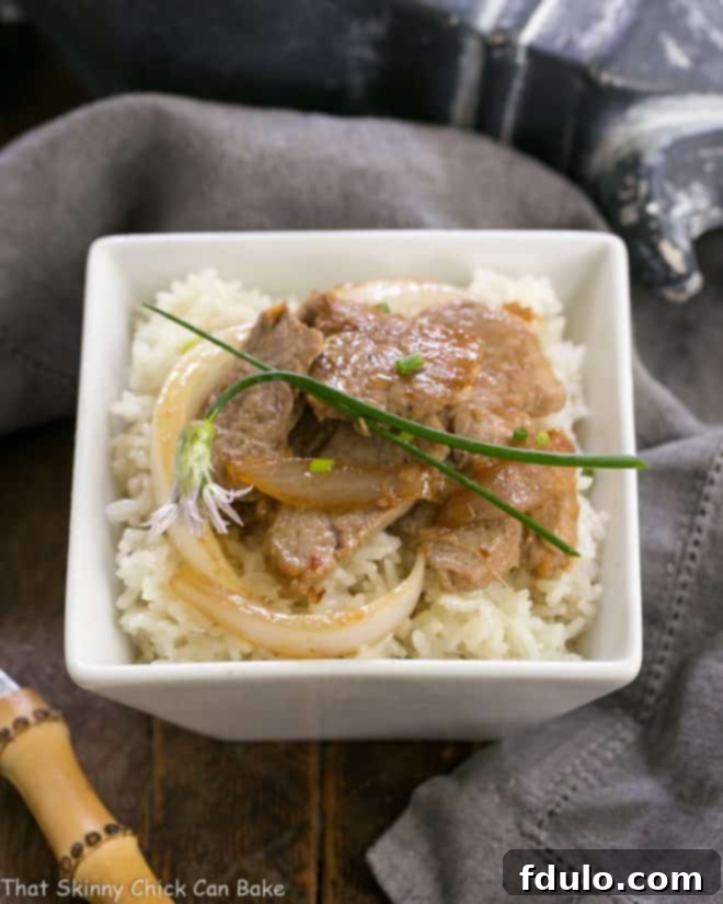 Korean stir fry - a marvelous Korean pork recipe with a bit of a kick! A close-up shot of Korean Stir Fry, rich with marinated pork and onions, served in a square white bowl over a bed of rice, highlighting the delicious textures and colors.