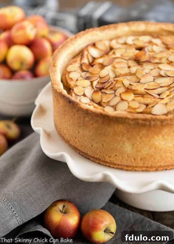Cream Cheese Apple Torte on a ruffled white ceramic cake stand with lady apples to garnish. A stunning centerpiece for any dessert table.