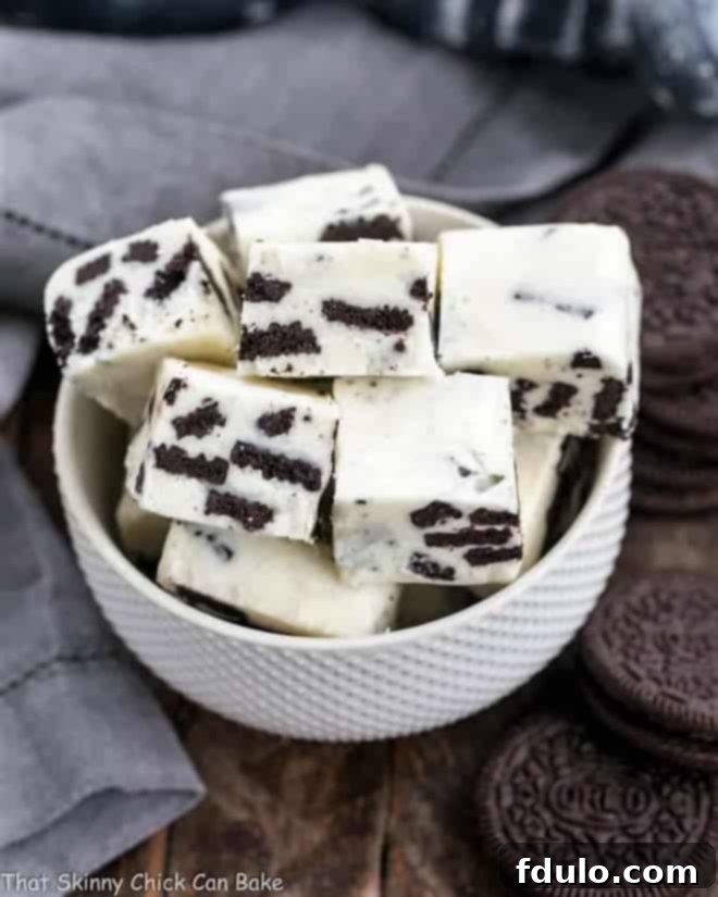 Squares of creamy white chocolate Oreo fudge, studded with cookie pieces, in a white bowl, ready to be enjoyed.
