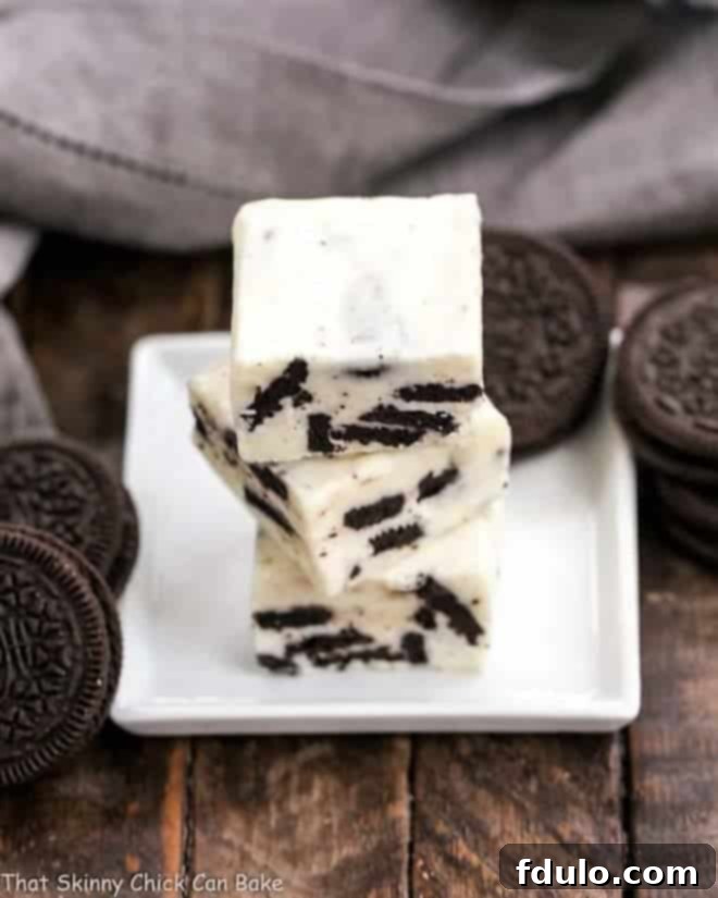 Stacked squares of luscious White Chocolate Oreo Fudge on a white square plate, showcasing the creamy texture and cookie bits.