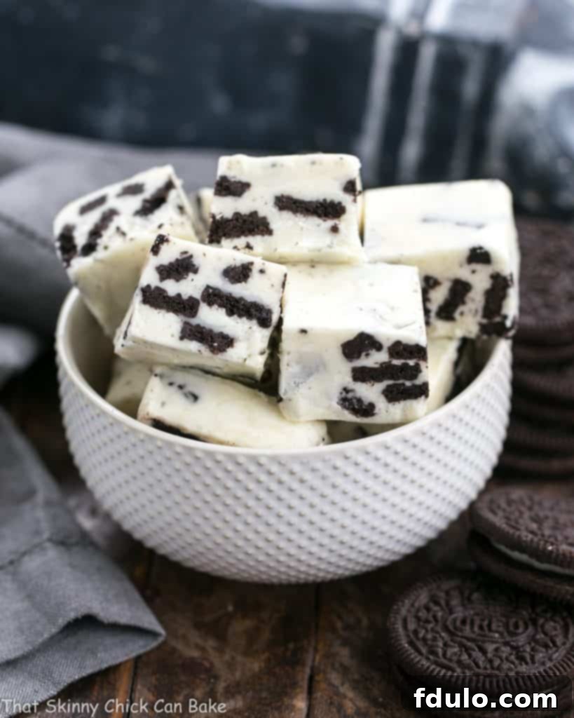 Close-up of Oreo White Chocolate Fudge squares in a white ceramic bowl, with whole Oreo cookies scattered around, highlighting the cookies and cream texture.