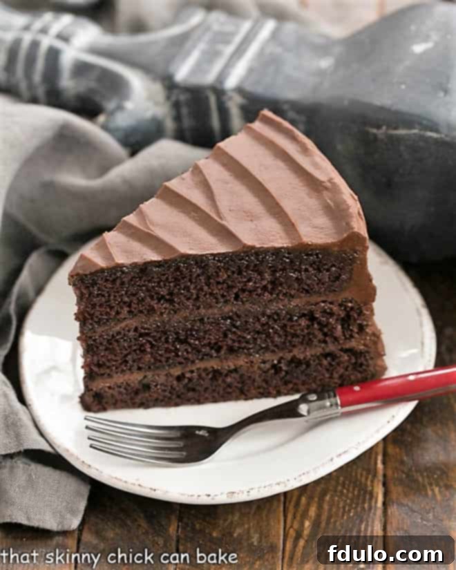 A delectable slice of Hershey's Chocolate Cake on a white dessert plate, accompanied by a vibrant red fork, showcasing its rich texture, three distinct layers, and generous frosting.