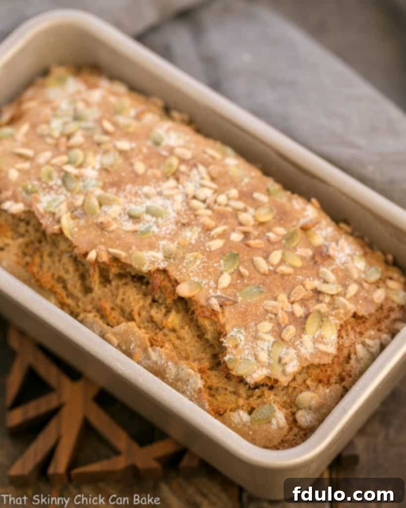 A freshly baked Seed-Topped Whole Wheat Banana Bread in a loaf pan, cooling on a wire rack.