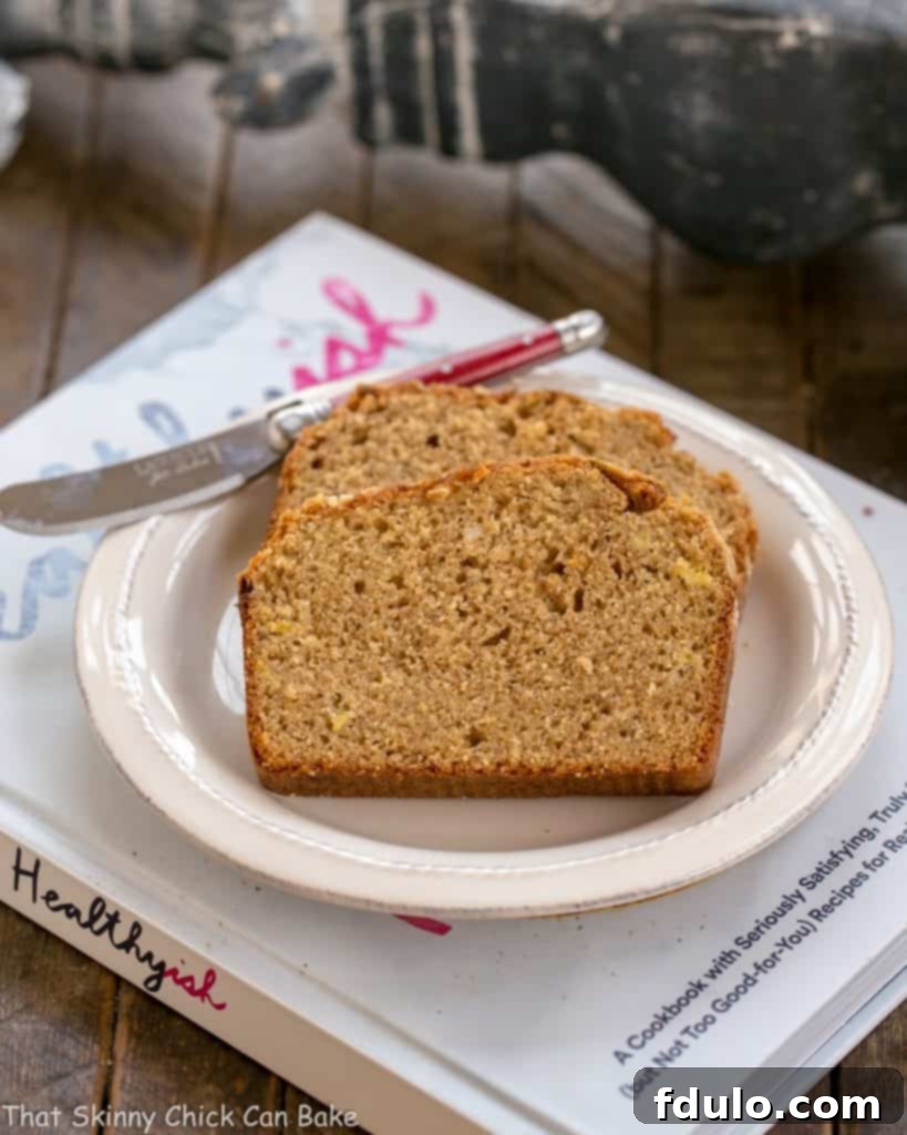 Two slices of Seed-Topped Whole Wheat Banana Bread resting on a white plate next to a cookbook, ready for a wholesome snack.