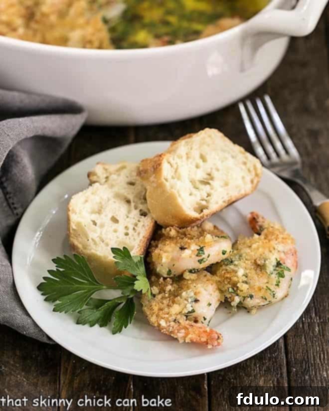 Easy Baked Garlic Shrimp - a quick, flavorful seafood dinner topped with crunchy breadcrumbs and a spicy garlic butter sauce. A serving of Baked Garlic Shrimp, golden-brown and topped with breadcrumbs, presented with crusty French bread slices on a small white plate, ready for dipping.